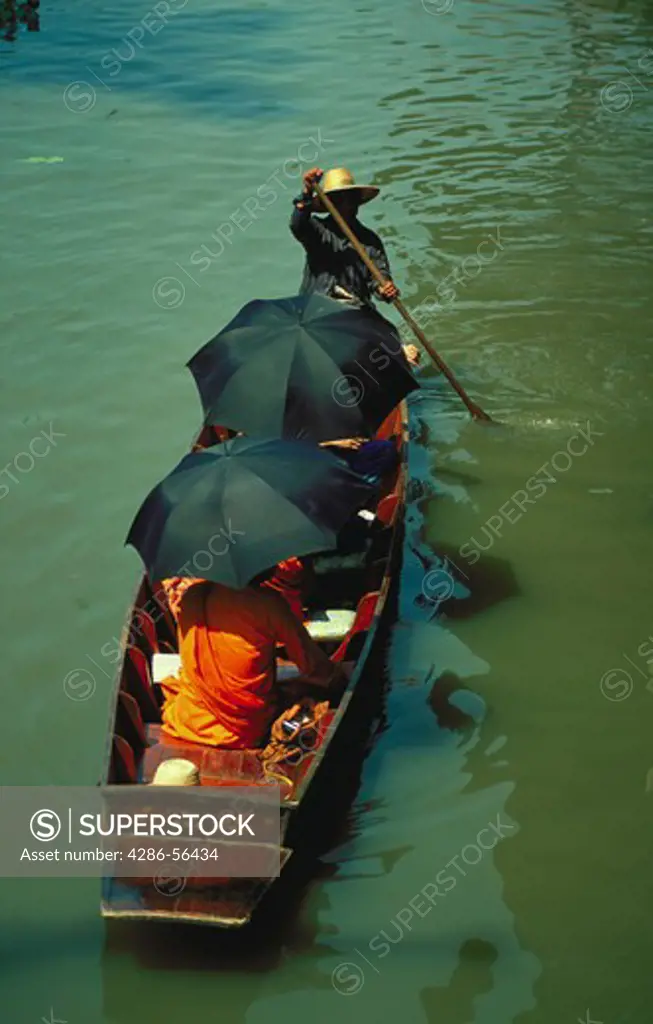 Monks shaded by umbrellas ride in a boat through a floating market in Thailand.