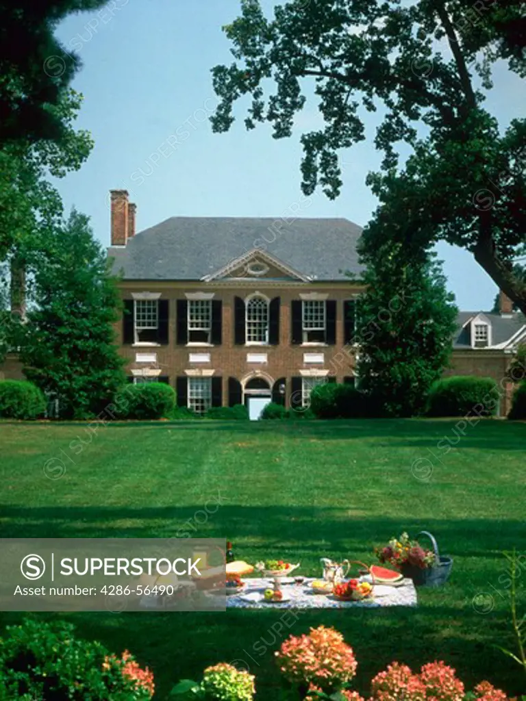 Portrait of the main hose at Woodlawn Plantation in Virginia with a large green lawn. In the foreground on the law a picnic blanket and lunch are set out. Property Release available.