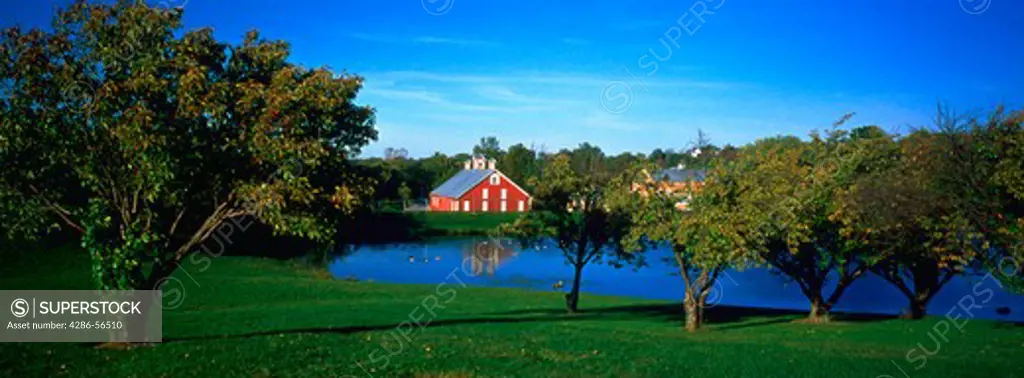 The pond at the Carroll County Farm Museum in Maryland surrounded by trees with a red barn in the background.