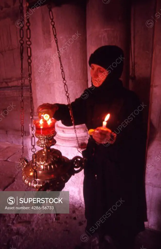Old woman pilgrim lighting candles inside The Church of the Holy Sepulchre. Jerusalem. Israel