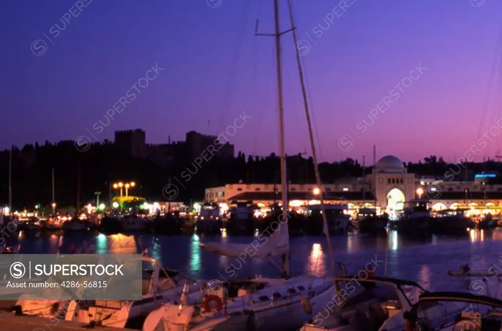 Greece. Rhodes New Town. Mandraki harbor at dusk showing the New Market and Palace of The Grand Masters.