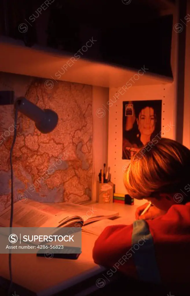 Young boy in his room sat at his desk and doing his homework.