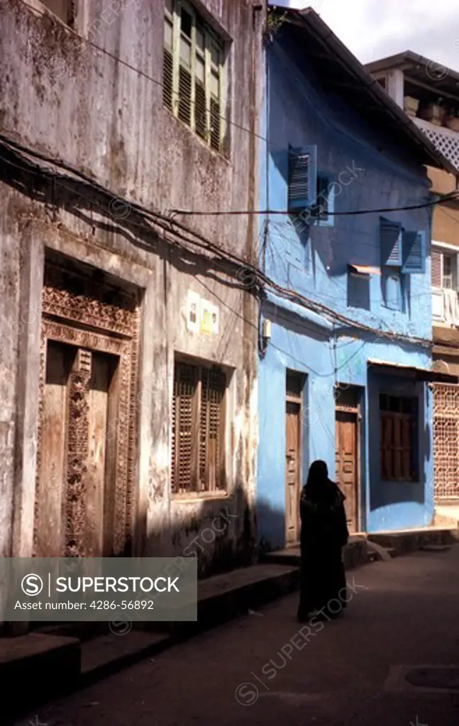 Zanzibar.Tanzania. Typical alleyway in Stone Town, showing the Old Carved Doors and Zanzibari woman wearing the tradional Khanga robes. 