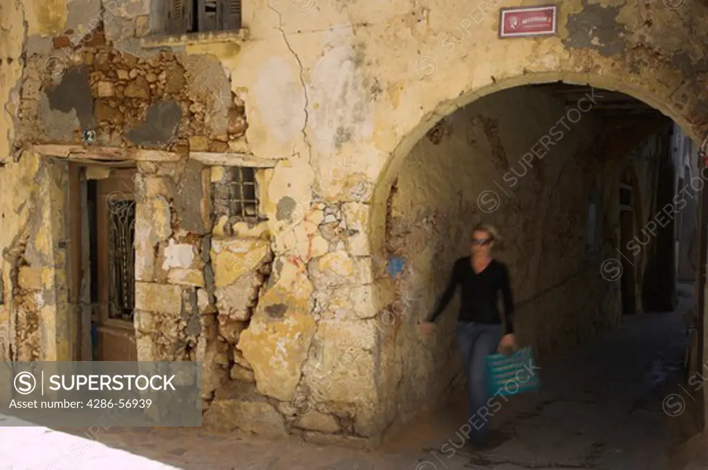 Greece. Western Crete. A young woman walking past a derelict Venetian House in Chania Old Town.