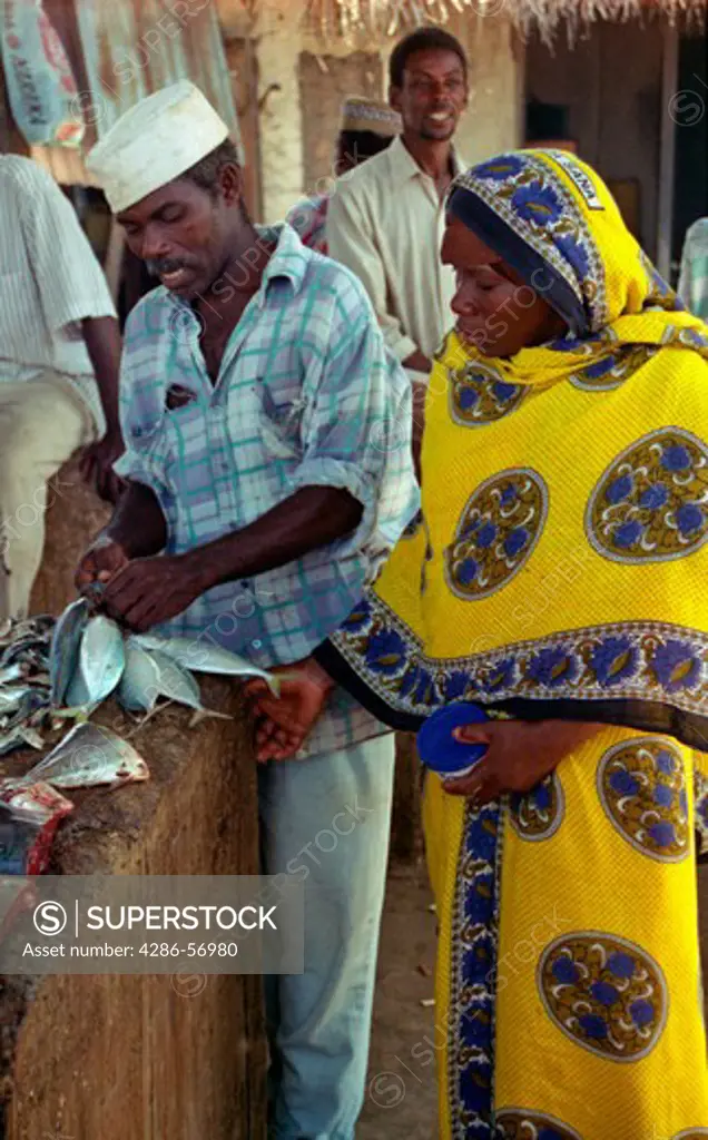 Zanzibar. Tanzania. East Africa. A young Zanzibari women wearing the traditional khanga, buying freshly caught fish at Mkotoni village fish market. 