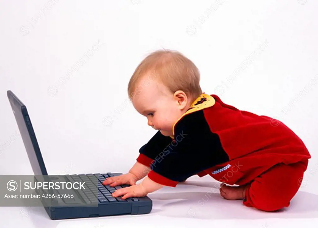 Profile view of a baby playing with a laptop computer.