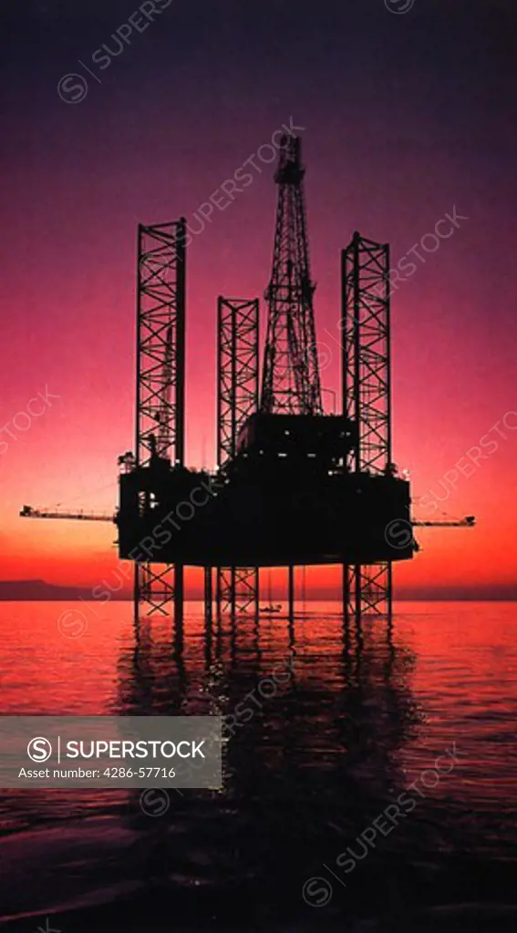 An off shore oil rig in the Gulf of Mexico silhouetted against a purple sunset.