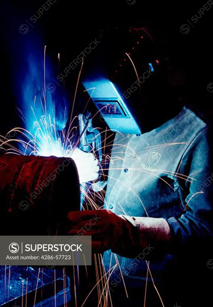 Manufacturing image of a welder in the process of welding metal with many sparks flying around his mask.