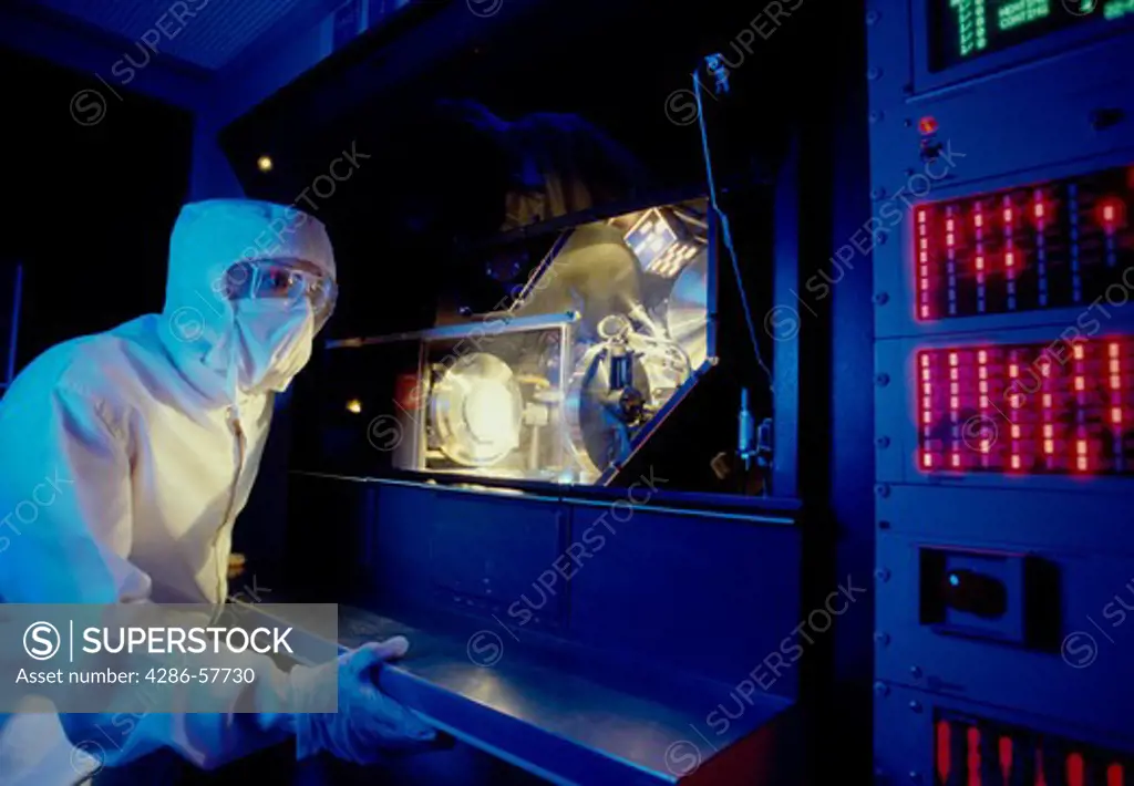A technician wearing a white clean suit working in a semiconductor wafer production plant in Silicon Valley, California.