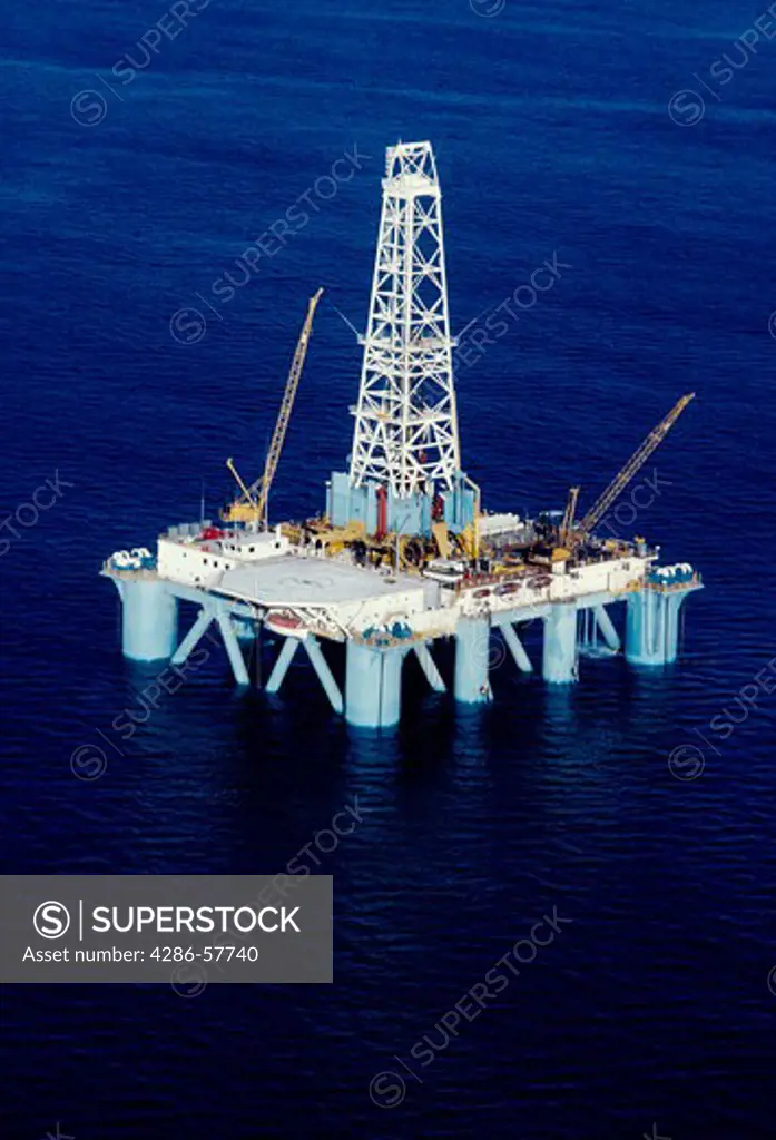An oil rig in the ocean containing several large cranes on board.