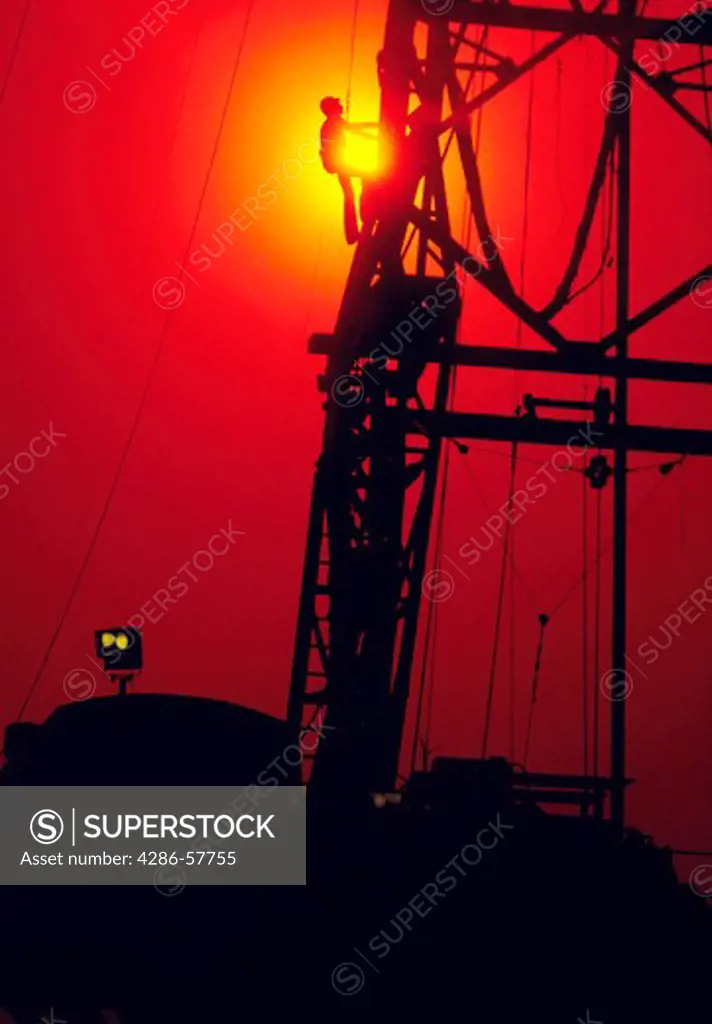 A man climbing up the side of an oil rig as the sun rises in the background, Houston, Texas.