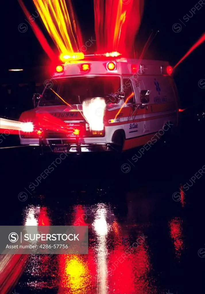 An evening image of an ambulance its lights that are reflecting onto the road.