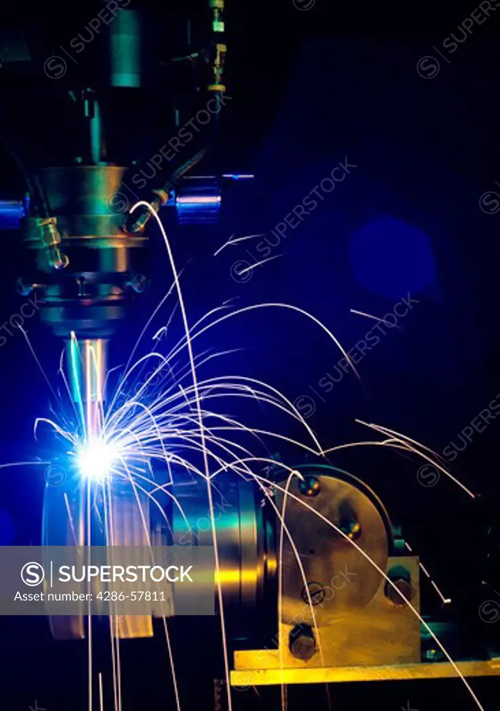 Sparks fly as a welding machine works on a stainless steel bar.