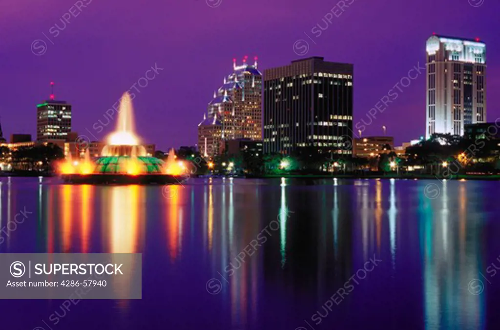 View at night of the lights of the Orlando, Florida skyline across Lake Eola with its spectacular fountain illuminated in the foreground.