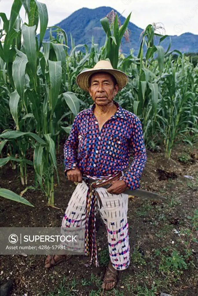 Mayan corn farmer wearing traditional hand woven clothing pauses under the San Pedro volcano near Lake Atitlan, San Pablo La Laguna, Guatemala