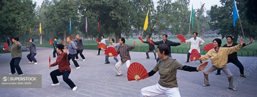 Red fans highlight group performing taichi exercises at sunrise, Temple of Heaven, Beijing, China