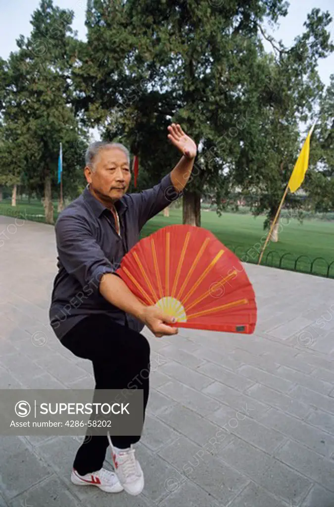Man with red fan performs taichi exercises at sunrise, Temple of Heaven, Beijing, China