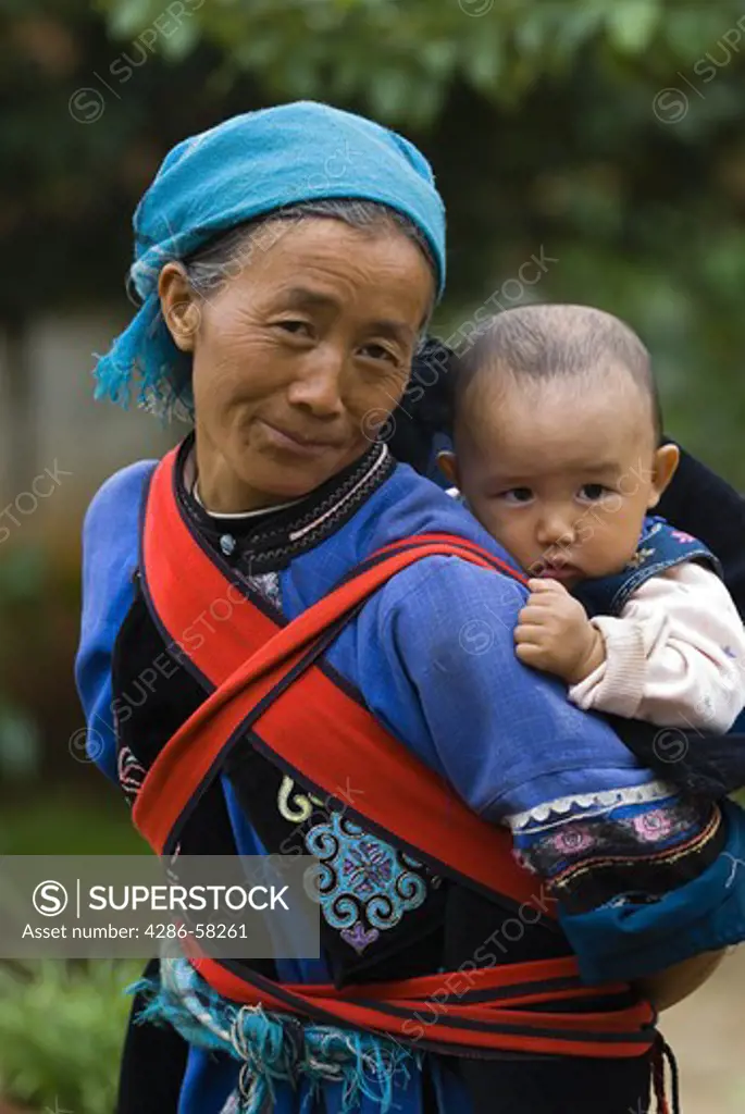Bi Fengying, dressed in costume of Sani ethnic minority, carries granddaughter, Azhuodi village, Shilin County, Yunnan, China.