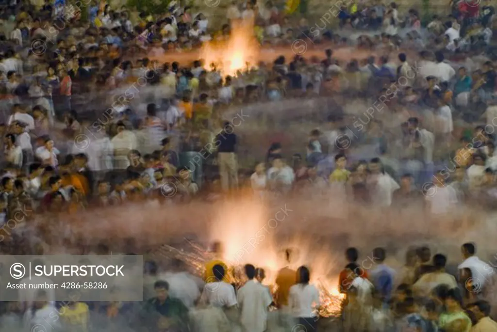 Creating solar systems of movement, audience members dance around bonfires at annual June Torch Festival, commemorating story of Sani ethnic minority saving crops from locusts with buring torches, Shilin, Yunnan Province, China.