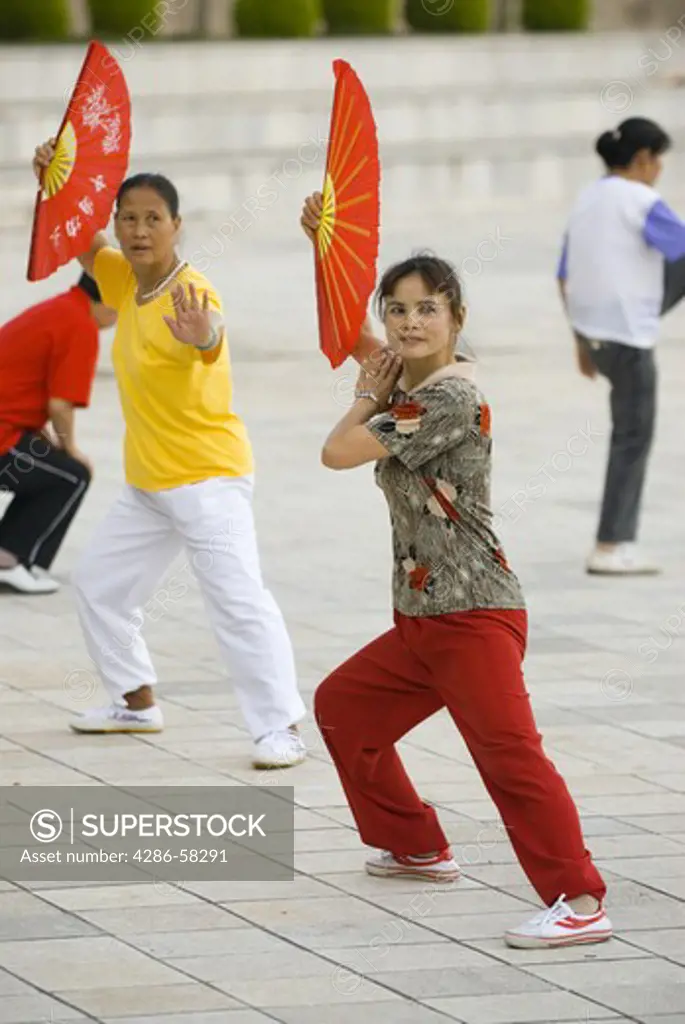 Middle aged women holding red fans perform predawn taichi exercies in city park, Geju, Honghe County, Yunnan Province, China.