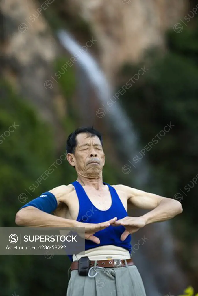 With waterfall as backdrop, senior performs predawn taichi exercies in city park, Geju, Honghe County, Yunnan Province, China.