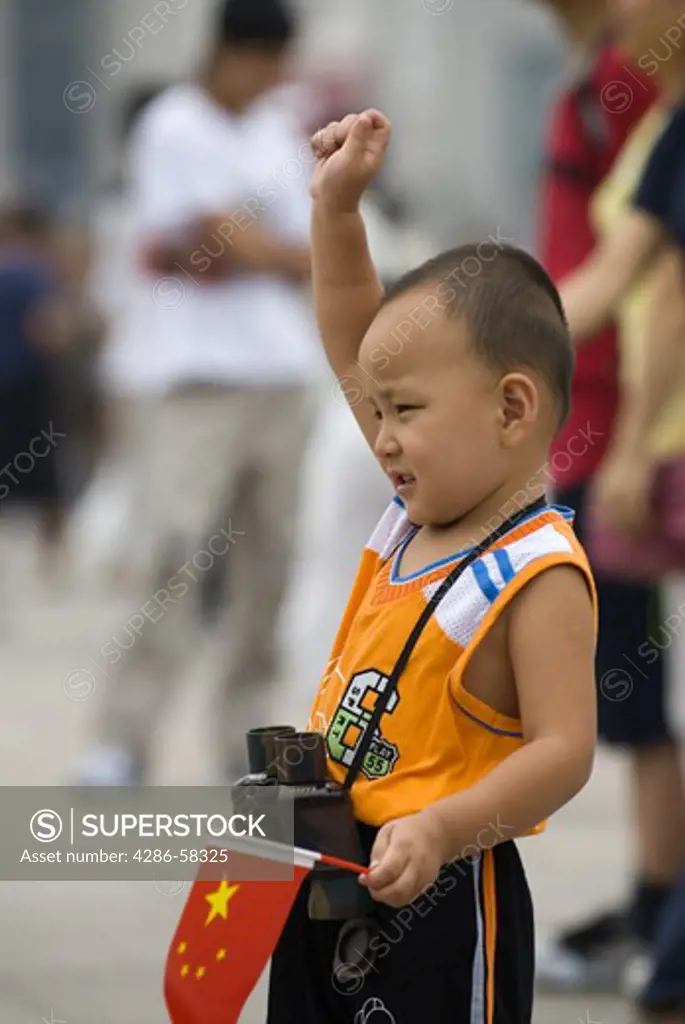 Wearing western sport clothes and posing for parent's snap shot, young boy salutes and hold's Chinese flag during outing at Tiananmen Square, Beijing, China.