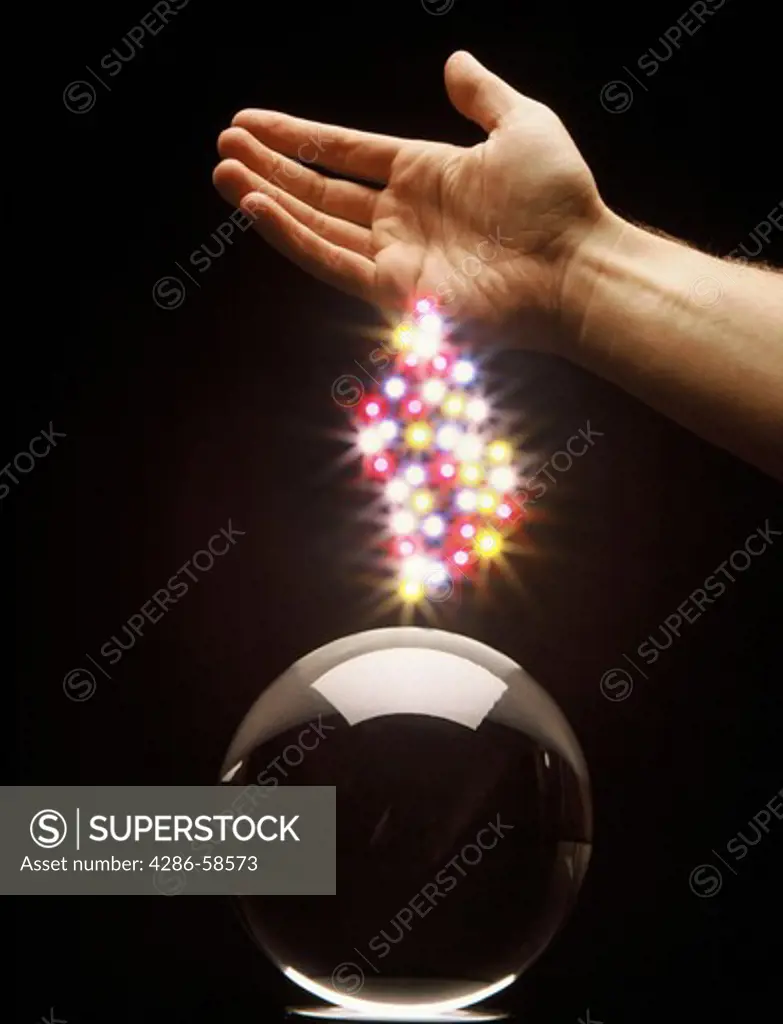 Hand with magic lights over crystal ball.