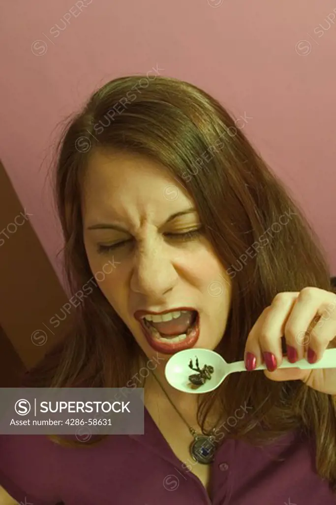 Young woman preparing to eat a dead bug from a plastic spoon.  MODEL  RELEASED.