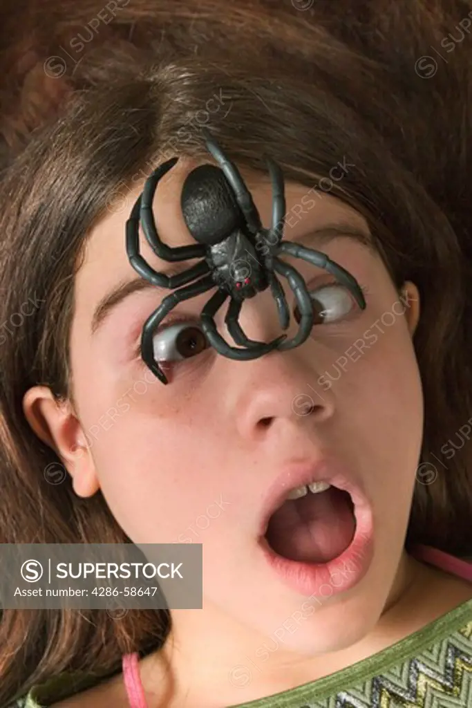 Girl posing with a fake rubber spider sitting on her forehead.  MODEL RELEASED.