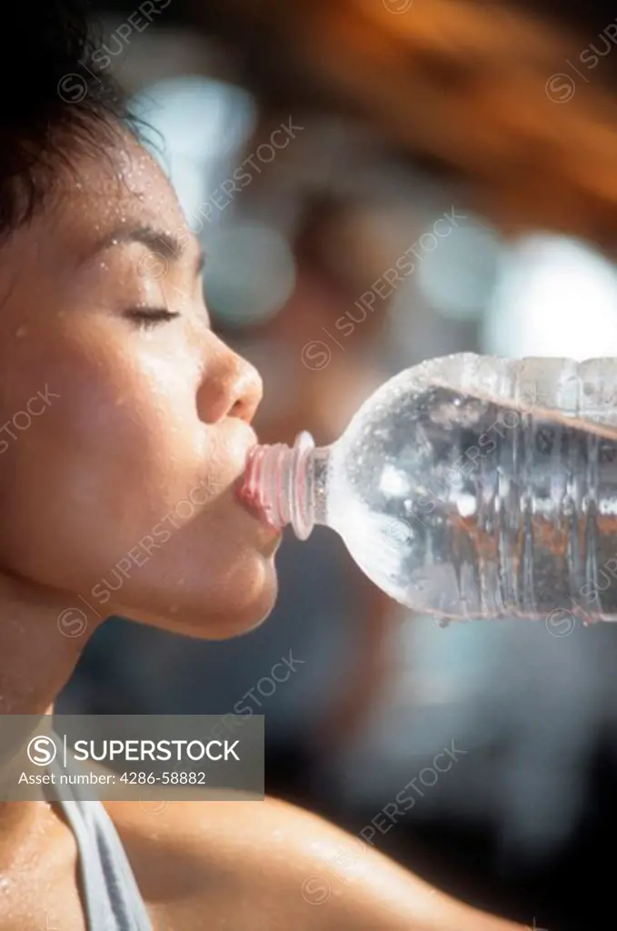 Asian woman drinks water during her exercises as gym.