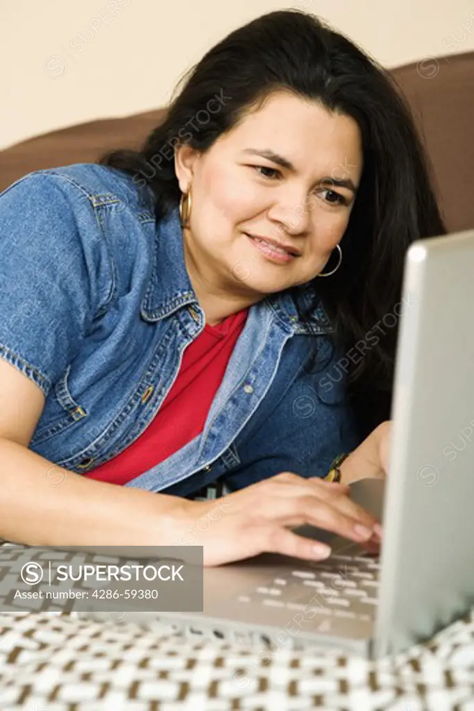 Mature woman lying on the bed and using a laptop