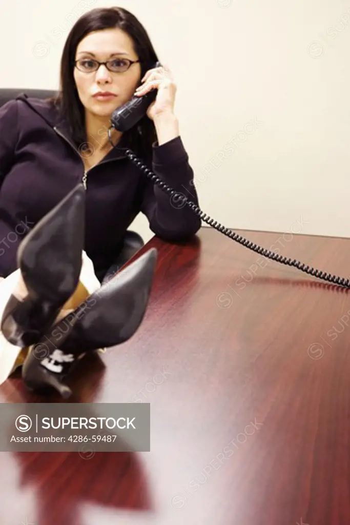 Portrait of a businesswoman talking on the telephone with her legs on a table