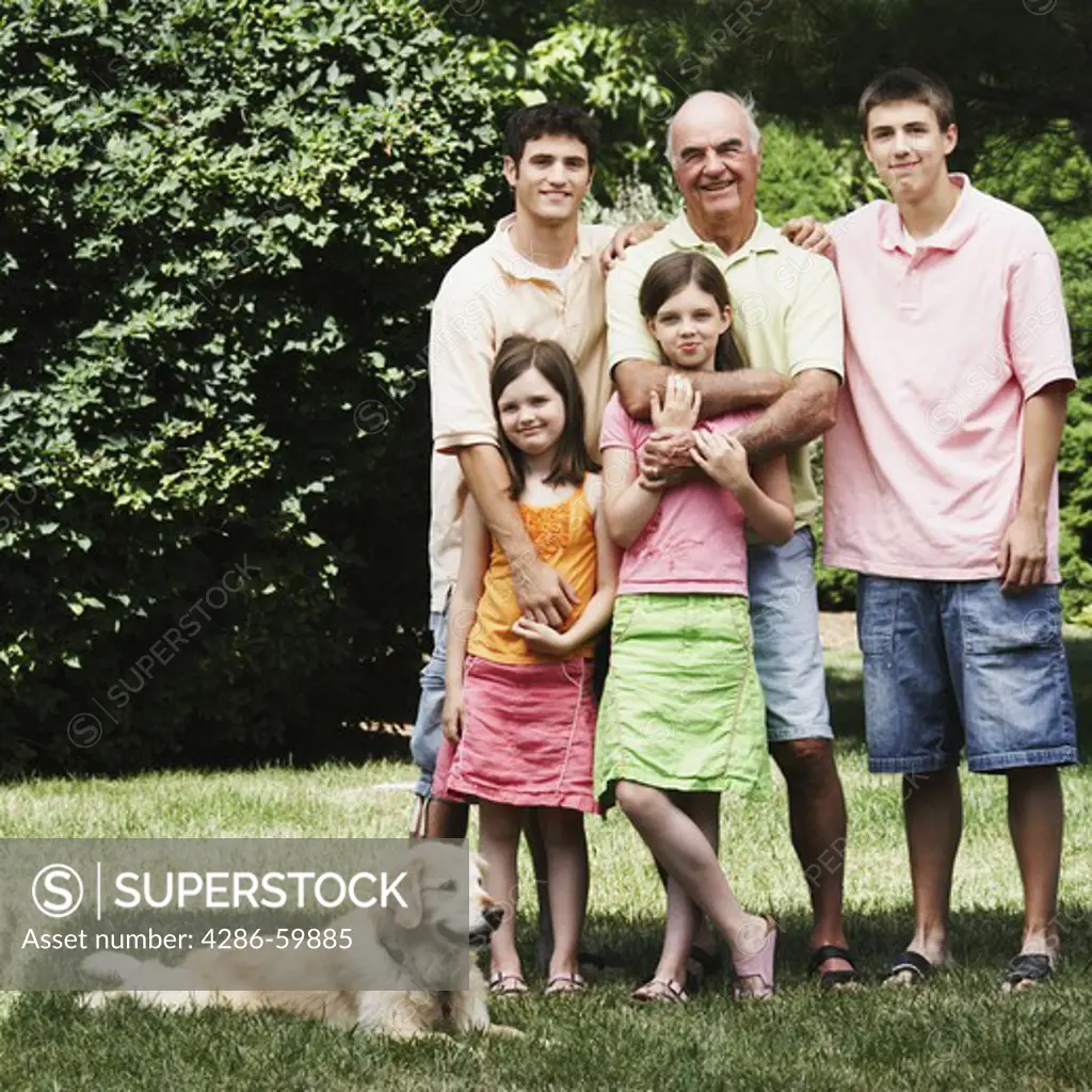 Senior man standing with his grandchildren and a dog in a park