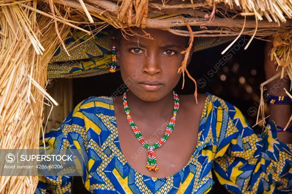 A Fulani girl stands in the doorway of a straw hut in the small village of Bele Kwara in southwestern Niger .  The Fulani people are primarily nomadic pastoralists who crisscross across the West African Sahel, leading their cattle, sheep, and goats in search of water and rich grazing grounds in a yearly cycle that has continued for centuries. In the past years, though, a large percentage of Fulani people have adopted a more sedentary lifestyle. While still holding onto their pastoralist roots, s