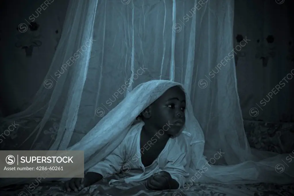 A child in the Garki area of Abuja peeks out from under a Permanet long lasting insecticide treated mosquito net.  Sleeping under a mosquito net every night prevents malaria, which is transmitted through the bite of an infected mosquito.  Globally, malaria kills 1,000,000 people every year, most of them pregnant women and children under five. NOT MODEL RELEASED. EDITORIAL USE ONLY.
