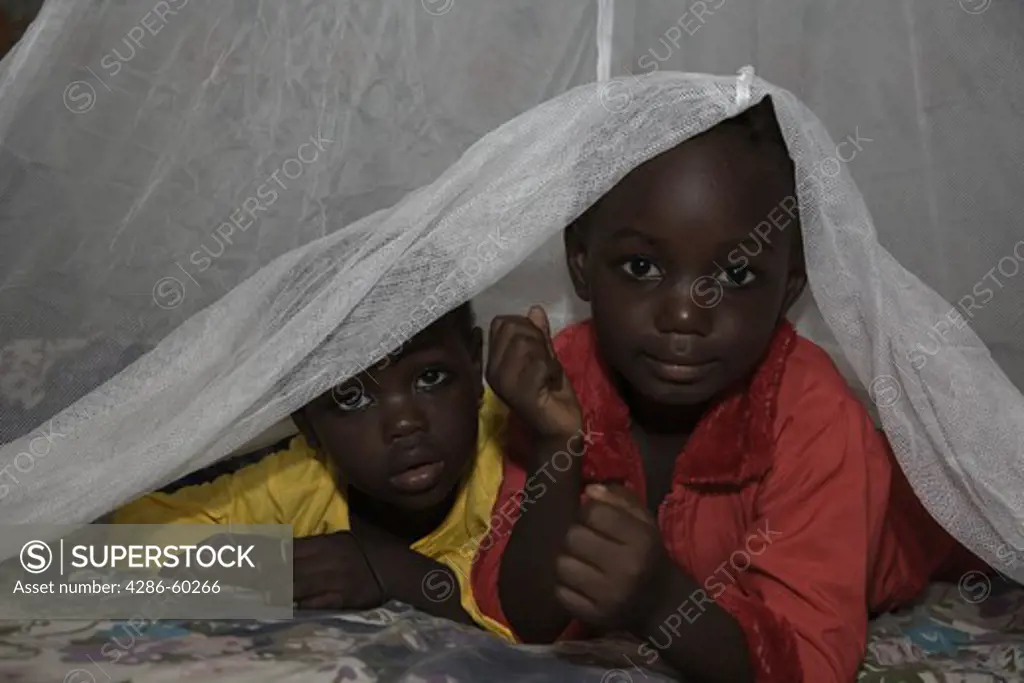 Two children peek out from under a Permanet long lasting insecticide treated mosquito net in the Garki area of Abuja. Sleeping under a mosquito net every night prevents malaria, which is transmitted through the bite of an infected mosquito.  Globally, malaria kills 1,000,000 people every year, most of them pregnant women and children under five. NOT MODEL RELEASED. EDITORIAL USE ONLY.