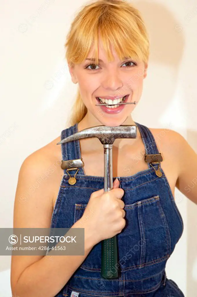 young DIY woman in overalls with hammer and nail