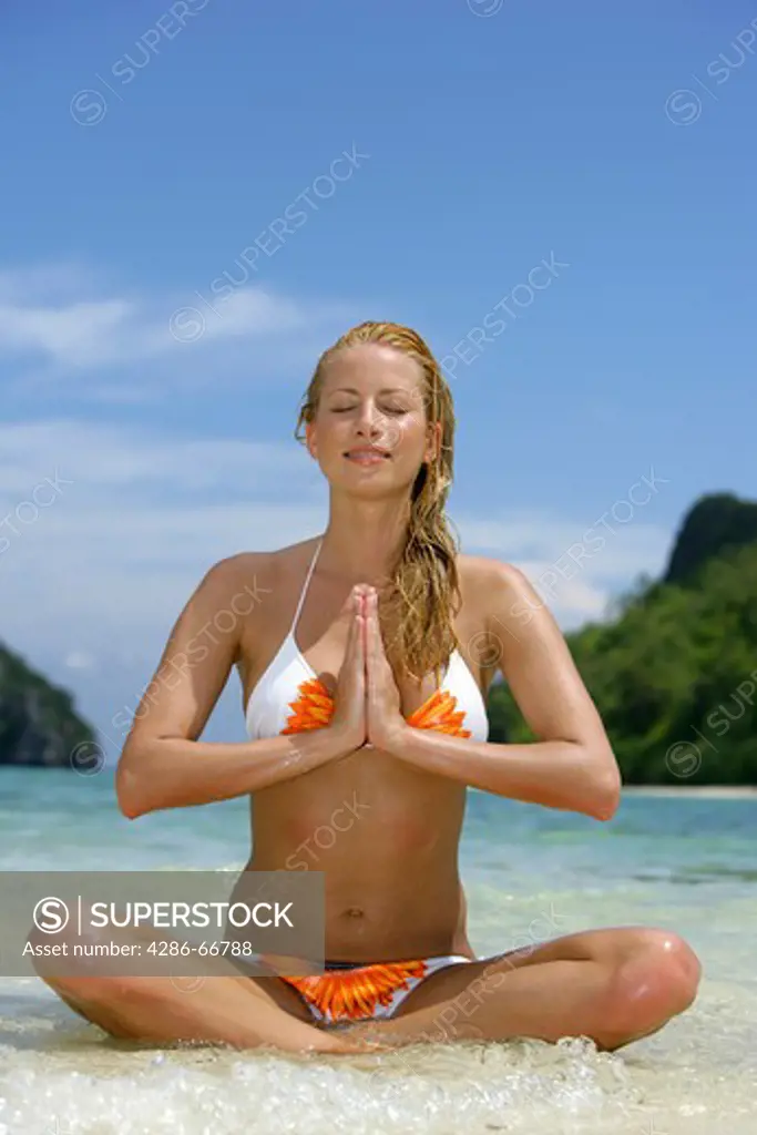 young blonde woman doing yoga on the tropical beach in