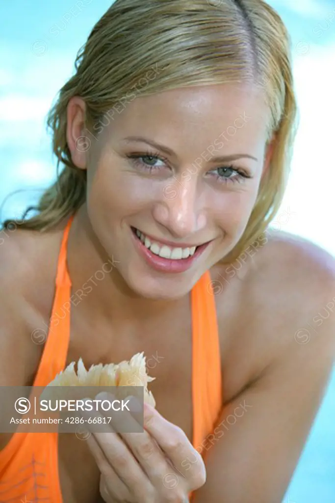 young blonde woman eating pomelo in summer holiday, portrait