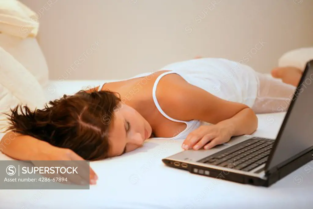 Young woman sleeping on bed with laptop