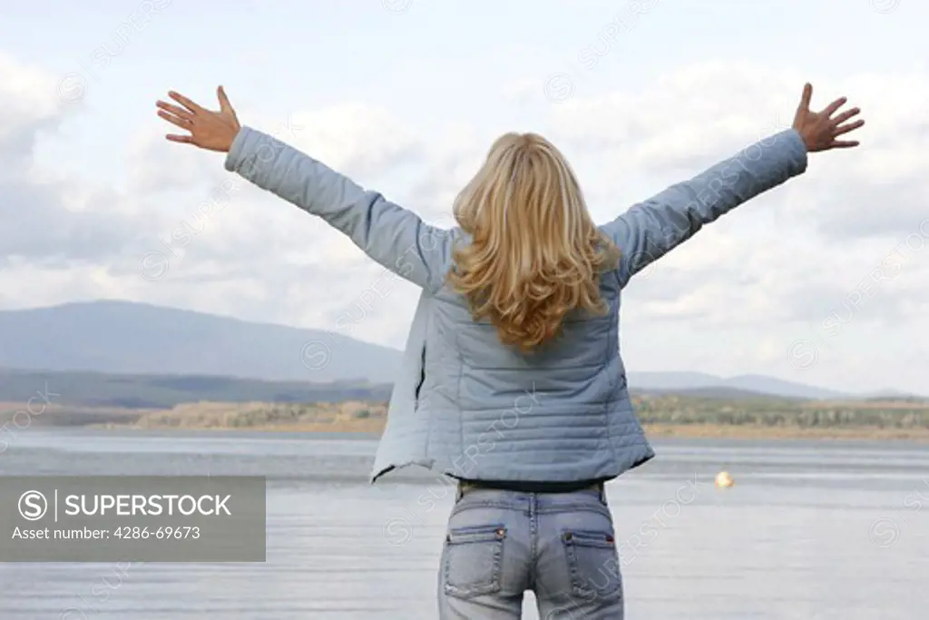 Woman stands with stretched out arms in a lake
