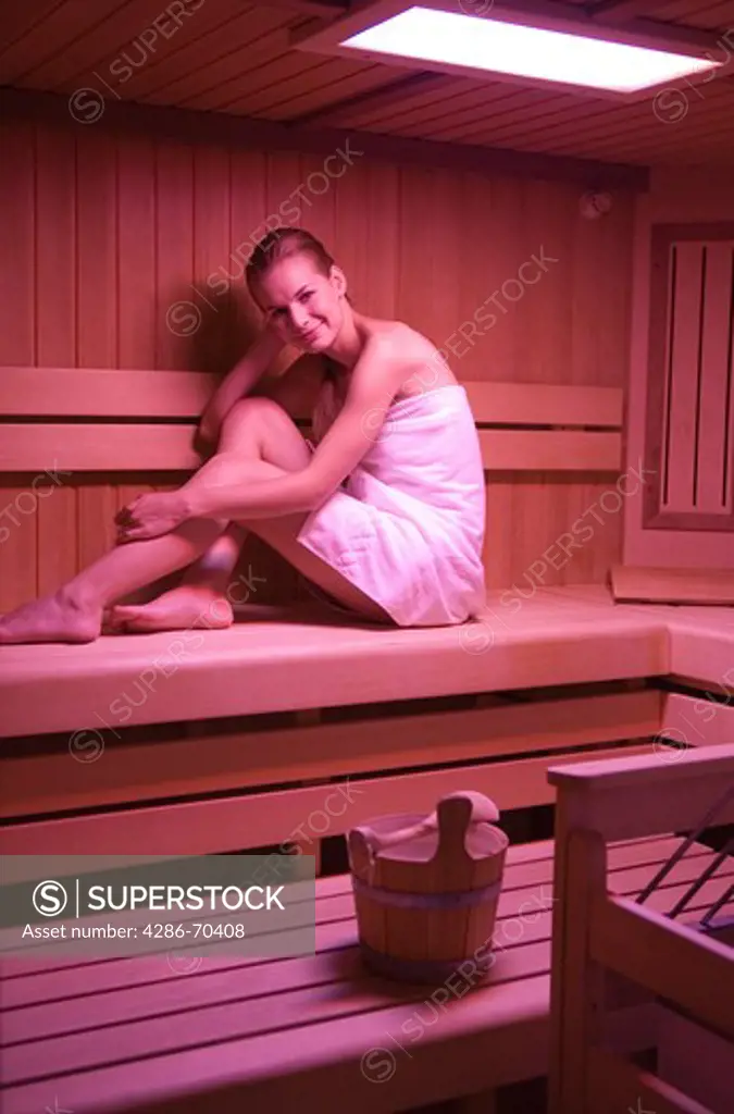 Young pretty woman sittinging in sauna. Red light stimulation. Colour theraphy.
