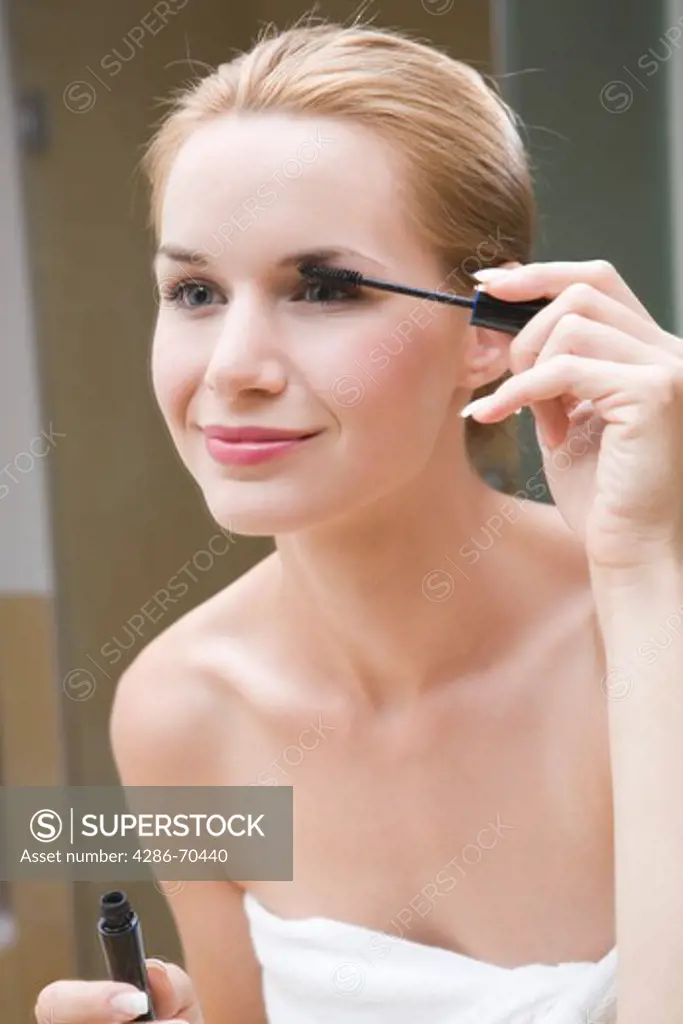 Young pretty woman doing makeup, using mascara.