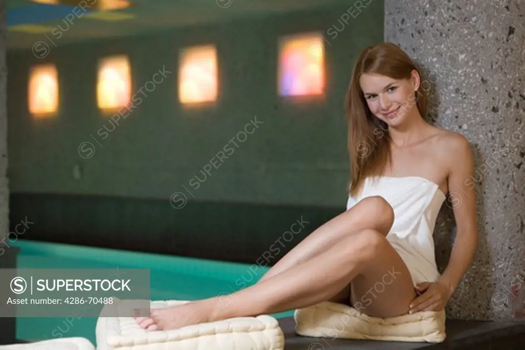 Young pretty woman sitting by the pool in wellness centre.