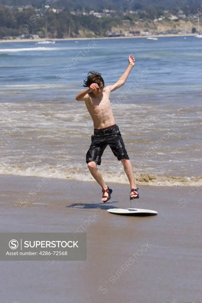 A young boy skim boarding on the beach on the Pacific Ocean in Santa Cruz, California