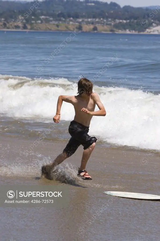 A young boy skim boarding on the beach on the Pacific Ocean in Santa Cruz, California