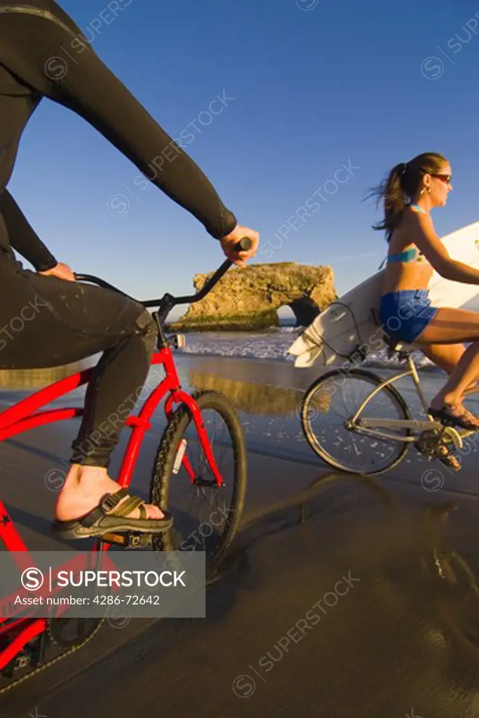 A woman on a cruiser bike riding past a man in a wetsuit on a cruiser bike at Natural Bridges State Park in Santa Cruz, California