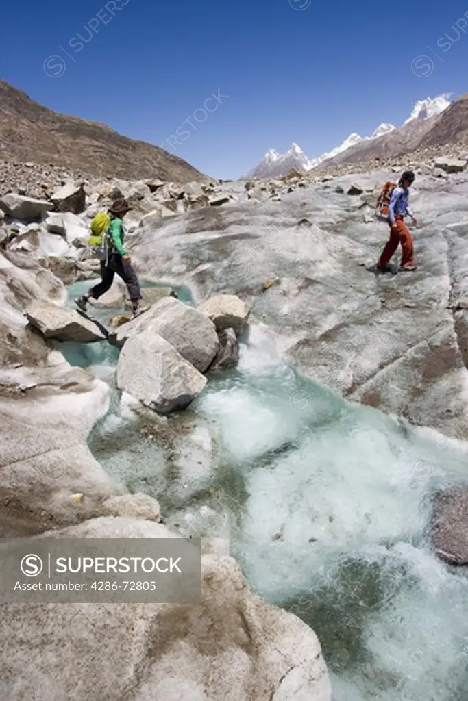  Two women crossing a stream on the Biafo glacier in the Karakoram Himalaya in Pakistan