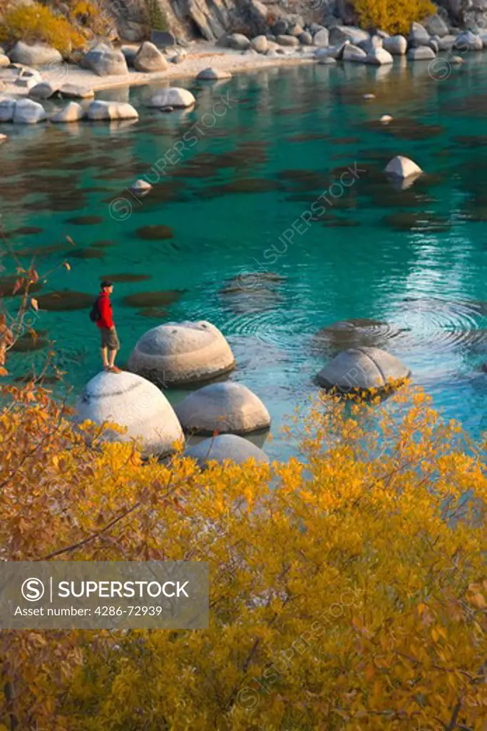  A man standing on a rock on the shore of Lake Tahoe in California at sunset with reflecting water