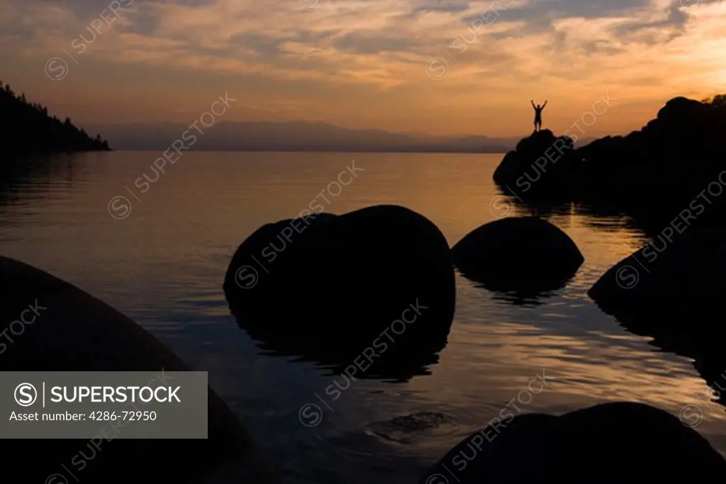  A man standing on a rock on the shore of Lake Tahoe in California at sunset with reflecting water